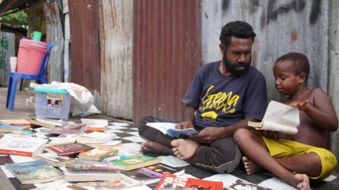
Pegiat Literasi, Mecky Tebai saat berbincang dengan seorang anak saat menggelar lapak baca di komplek Mapiduba. (Foto: Kristin Rejang/Sasagupapua)