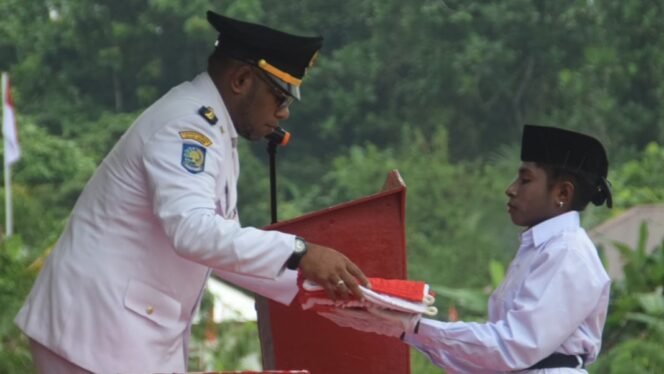 
Kepala Distrik Mimika Barat Jauh, Ever Kukuareyau saat menyerahkan bendera kepada pembawa baki Paskibra dalam momen upacara HUT ke-81 RI, Jumat (17/8/2026). Foto: Dok DMBJ. 